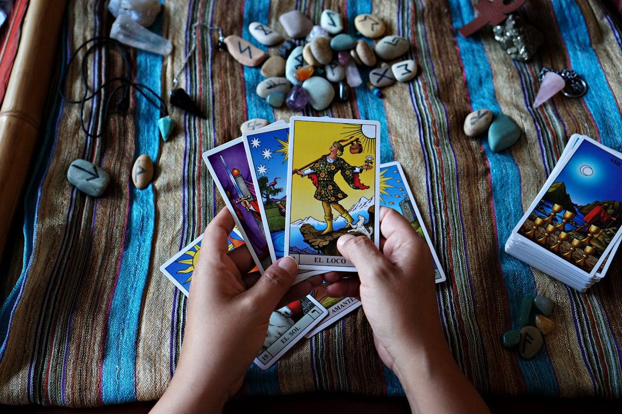 Close-up of hands holding tarot cards on a cloth, surrounded by runestones and crystals.